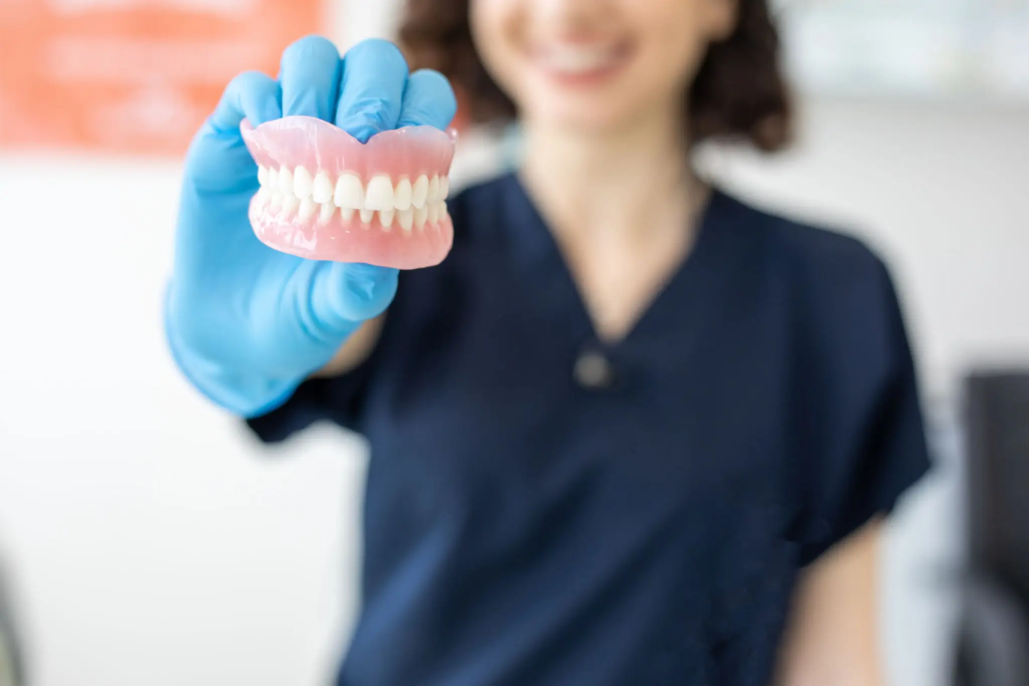A dentist holding a dental model with blue gloves.