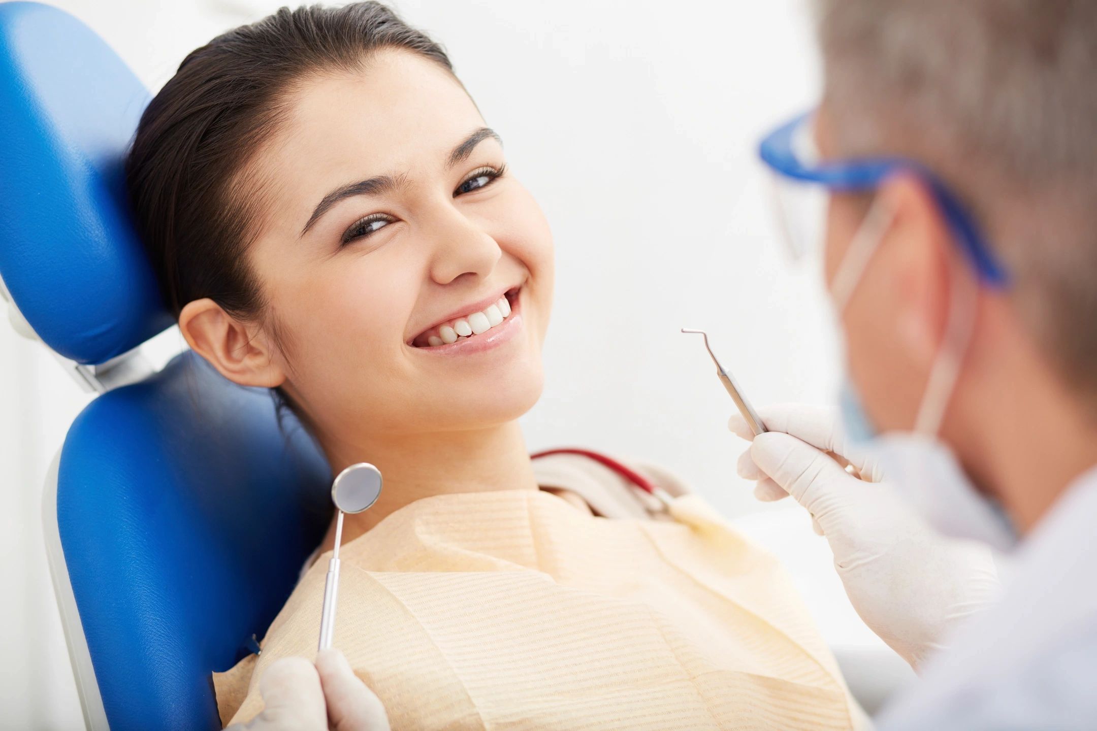 A smiling woman at the dentist's office holding a dental mirror.