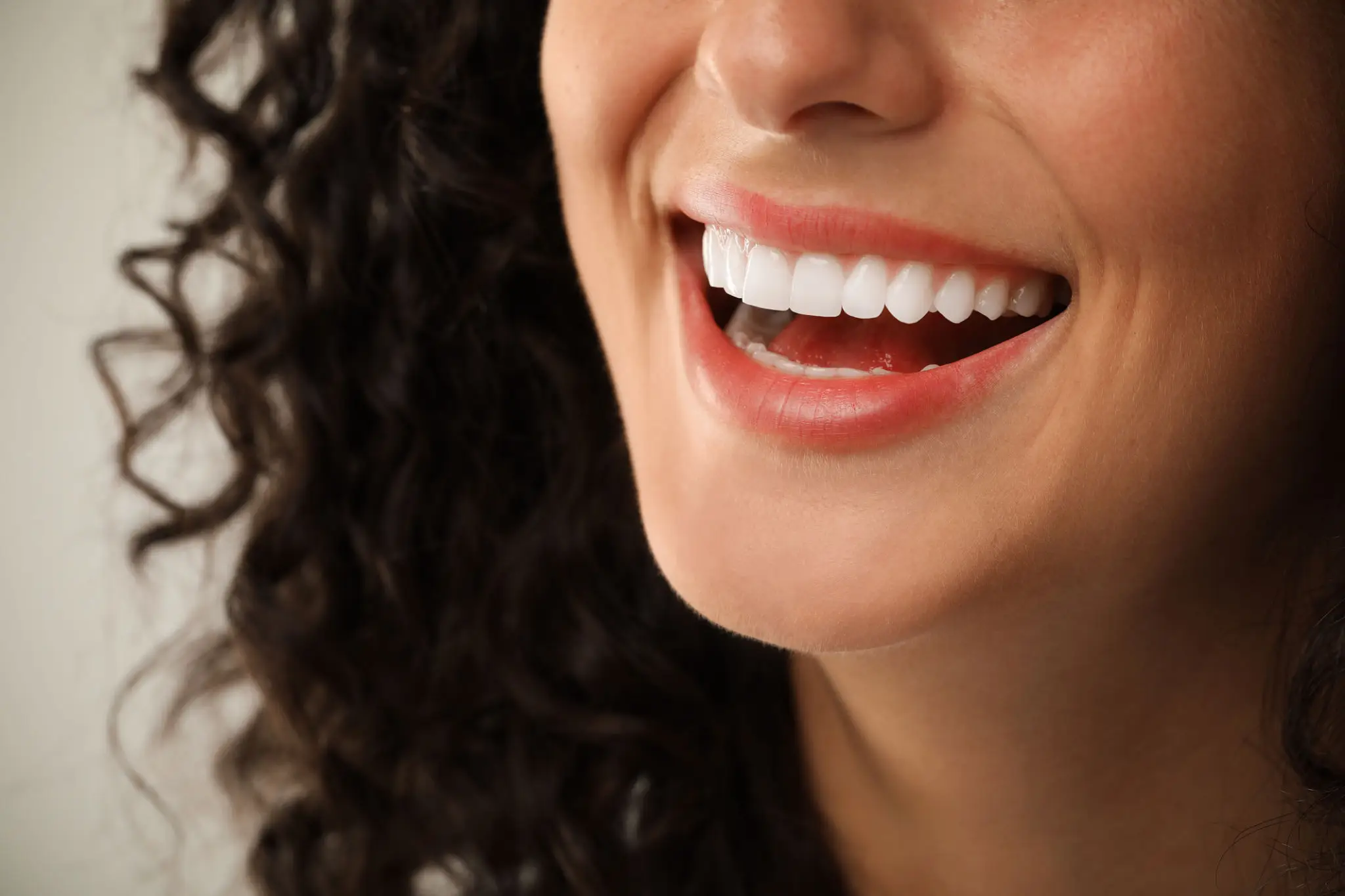 Close-up of a smiling woman with curly hair and white teeth.