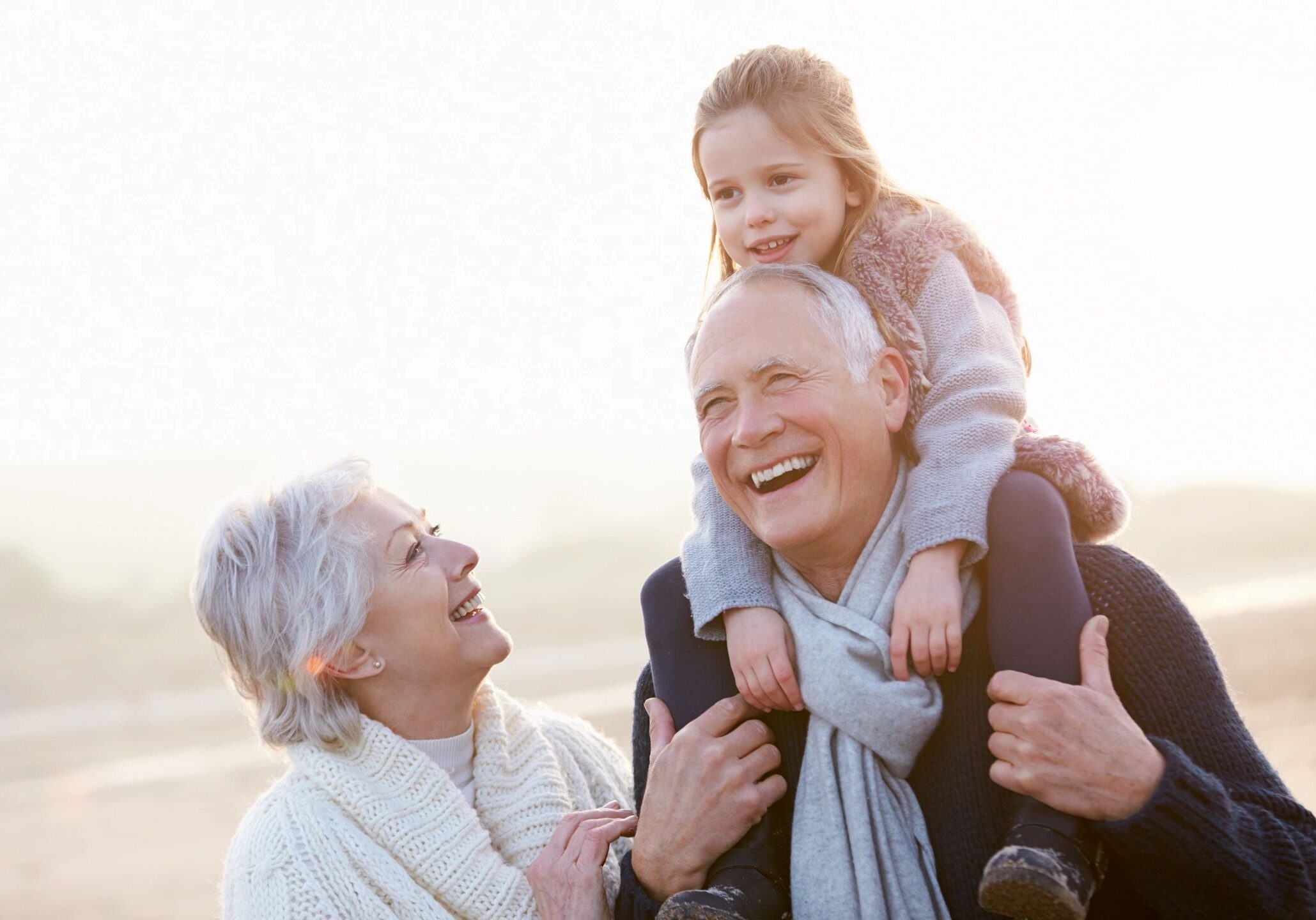 Elderly couple joyfully playing with their granddaughter outdoors.
