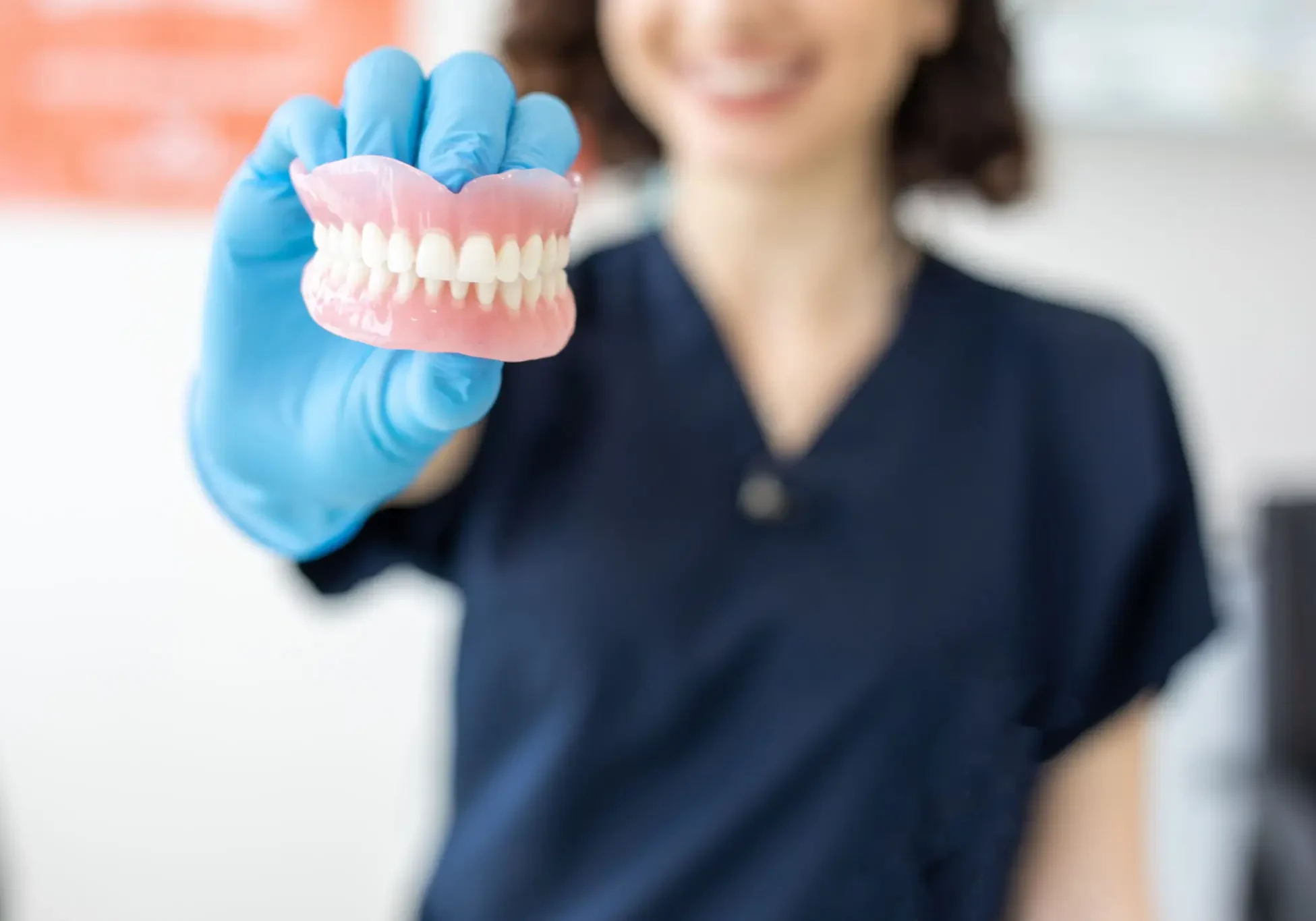 Dentist holding a model of teeth wearing blue gloves.
